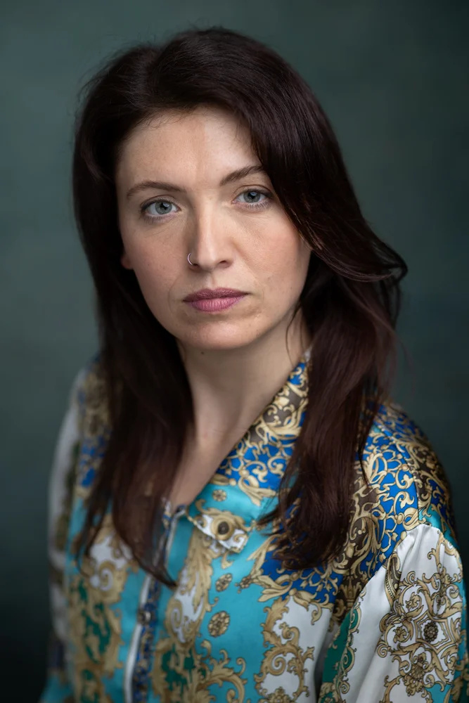headshots - a female actor with long dark hair and wearing a paisley top in front of a light green background